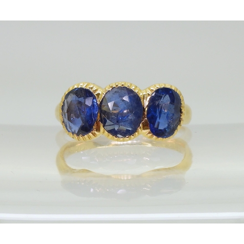 712 - A three stone sapphire ring, mounted in bright yellow metal, in pretty cut back bezel settings, fing... 