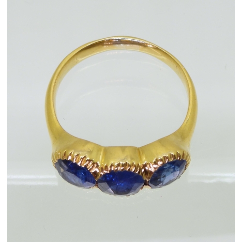 712 - A three stone sapphire ring, mounted in bright yellow metal, in pretty cut back bezel settings, fing... 