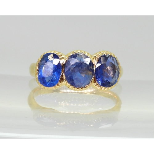 712 - A three stone sapphire ring, mounted in bright yellow metal, in pretty cut back bezel settings, fing... 