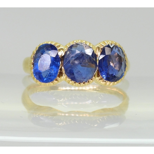 712 - A three stone sapphire ring, mounted in bright yellow metal, in pretty cut back bezel settings, fing... 