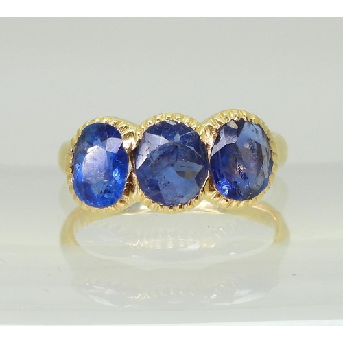 712 - A three stone sapphire ring, mounted in bright yellow metal, in pretty cut back bezel settings, fing... 