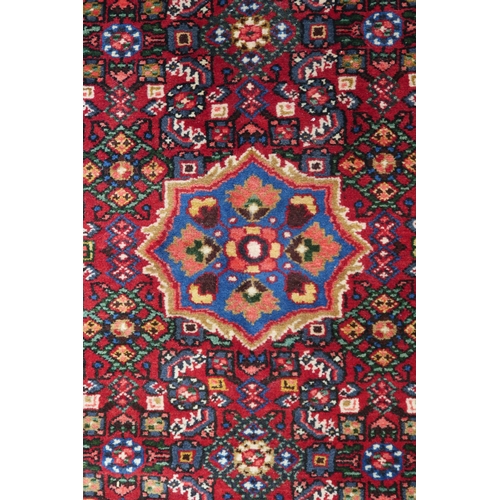 87 - A red ground Hamadan rug with blue central medallion, matching spandrels and multicoloured borders, ... 