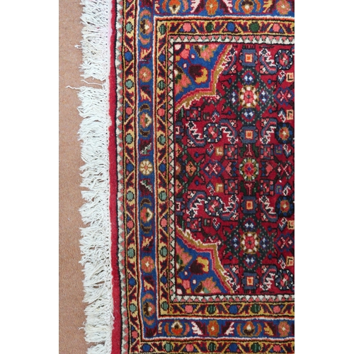 87 - A red ground Hamadan rug with blue central medallion, matching spandrels and multicoloured borders, ... 