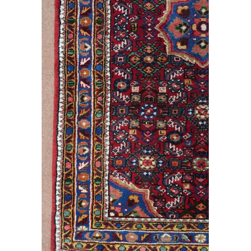 87 - A red ground Hamadan rug with blue central medallion, matching spandrels and multicoloured borders, ... 