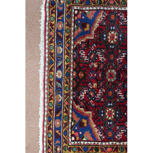 87 - A red ground Hamadan rug with blue central medallion, matching spandrels and multicoloured borders, ... 