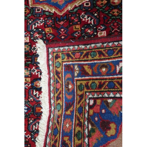 87 - A red ground Hamadan rug with blue central medallion, matching spandrels and multicoloured borders, ... 