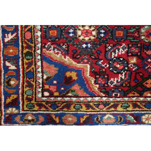 87 - A red ground Hamadan rug with blue central medallion, matching spandrels and multicoloured borders, ... 