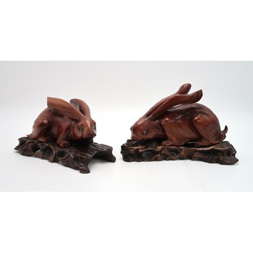 2310 - A PAIR OF CHINESE CARVED WOOD HARES each recumbent on pierced foliate and rocky bases, glass eyes, 2... 