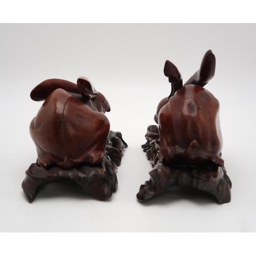 2310 - A PAIR OF CHINESE CARVED WOOD HARES each recumbent on pierced foliate and rocky bases, glass eyes, 2... 