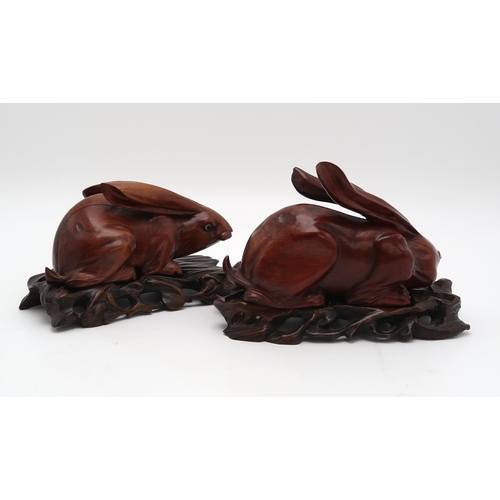 2310 - A PAIR OF CHINESE CARVED WOOD HARES each recumbent on pierced foliate and rocky bases, glass eyes, 2... 