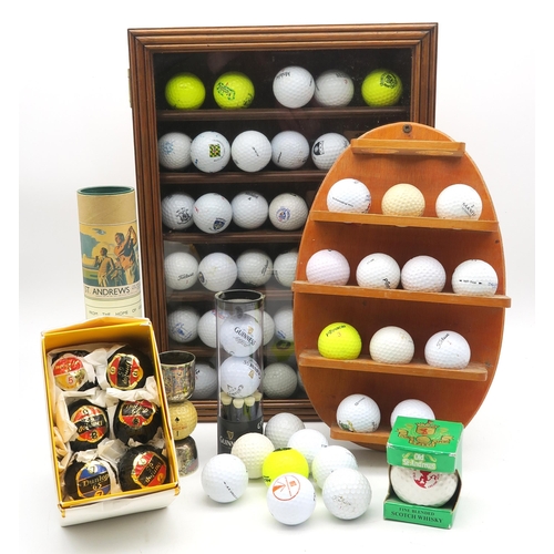 571 - A collection of golf balls, housed over a wall mounted rack and a glazed display case, including six... 