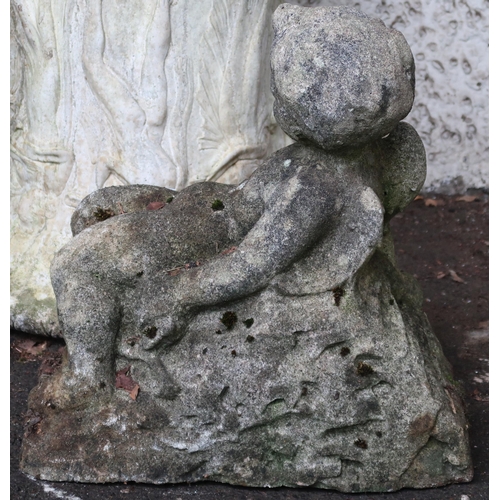 135 - A reconstituted stone garden statue of a reclining cherub, 48cm high x 46cm wide x 29cm deep