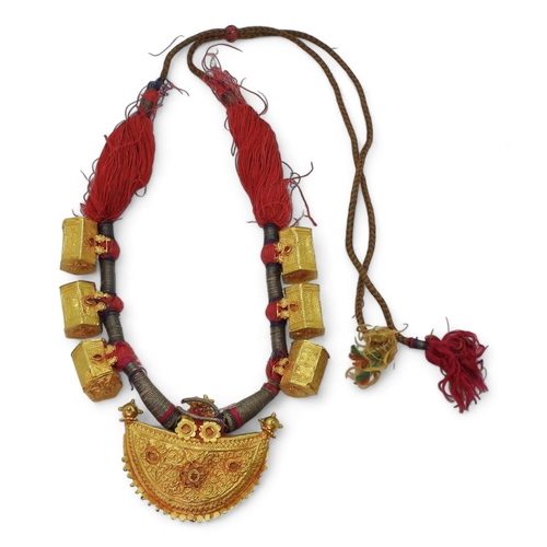 An antique Indian bridal necklace, in bright yellow metal the front half moon shaped pendant is embossed and chased with all over floral and diamond pattern motifs, with flower finials, with six hexagonal shaped beads also with flower details, all of them strung on the traditional red cord with gold thread. Dimensions of the front panel 7.6cm x 5.7cm, hexagonal beads 2.3cm x 2cm approx with loops., weight all together approx 93.8gms
