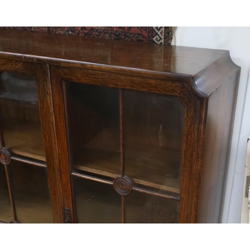 114 - A 20th century oak glazed bookcase with three beaded glazed doors on turned supports joined by stret... 