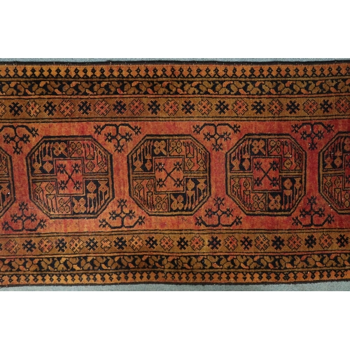 127 - A terracotta ground Bokhara style runner with six octagonal style medallions with multiple borders, ... 