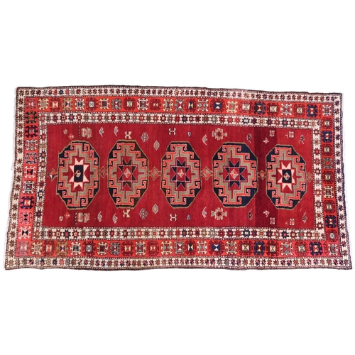 2122 - A RED GROUND CAUCASIAN RUNNER with five octagonal geometric medallions within orange and cream ... 