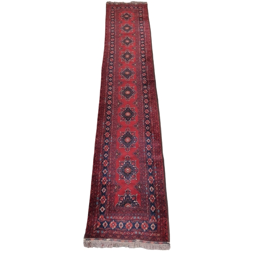 2125 - A RED GROUND FINE AFGHAN RUNNER with multiple dark medallions with multicoloured geometric bord... 