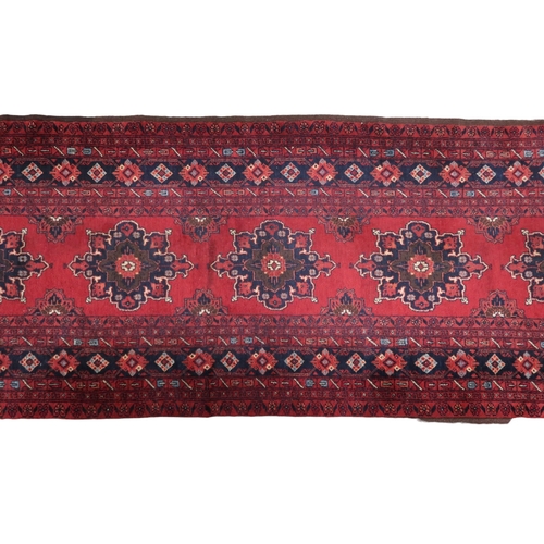 2125 - A RED GROUND FINE AFGHAN RUNNER with multiple dark medallions with multicoloured geometric bord... 