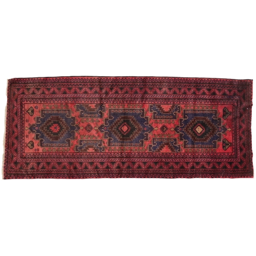 2128 - A RED GROUND AFGHAN TRIBAL BALUCHI RUNNER with three dark blue geometric medallions within mult... 