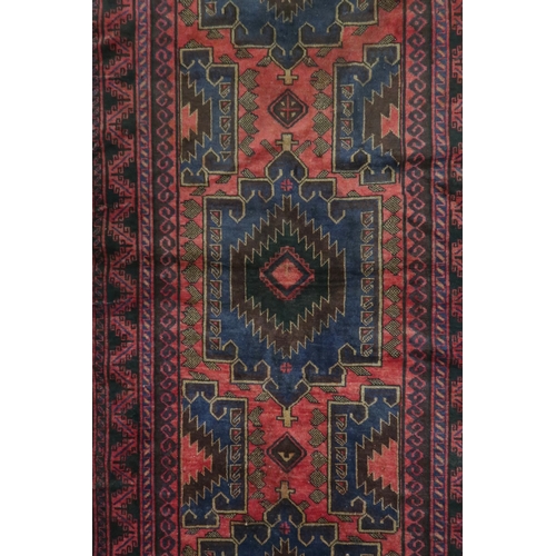 2128 - A RED GROUND AFGHAN TRIBAL BALUCHI RUNNER with three dark blue geometric medallions within mult... 