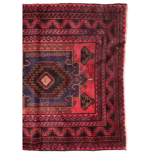 2128 - A RED GROUND AFGHAN TRIBAL BALUCHI RUNNER with three dark blue geometric medallions within mult... 