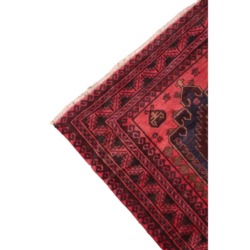 2128 - A RED GROUND AFGHAN TRIBAL BALUCHI RUNNER with three dark blue geometric medallions within mult... 