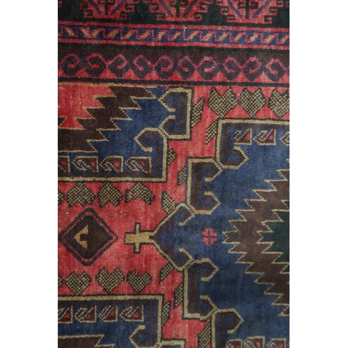 2128 - A RED GROUND AFGHAN TRIBAL BALUCHI RUNNER with three dark blue geometric medallions within mult... 