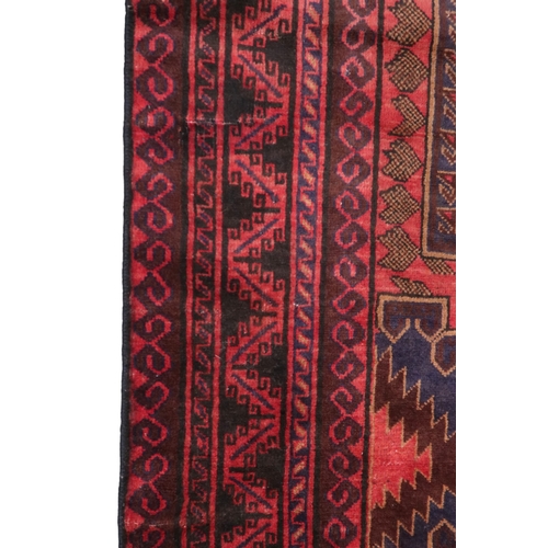 2128 - A RED GROUND AFGHAN TRIBAL BALUCHI RUNNER with three dark blue geometric medallions within mult... 