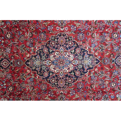 2130 - A RICH RED GROUND PERSIAN KASHAN RUG with dark blue floral patterned central medallion and matc... 