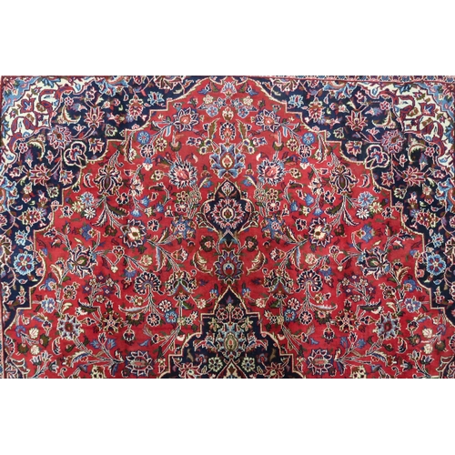 2130 - A RICH RED GROUND PERSIAN KASHAN RUG with dark blue floral patterned central medallion and matc... 