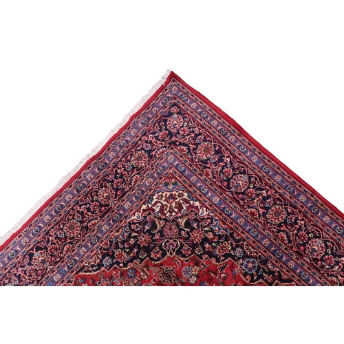 2130 - A RICH RED GROUND PERSIAN KASHAN RUG with dark blue floral patterned central medallion and matc... 