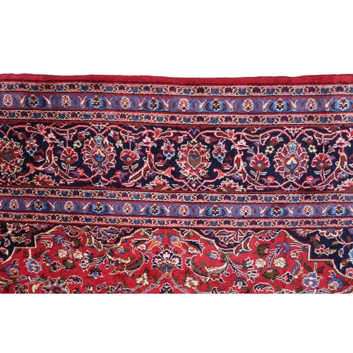 2130 - A RICH RED GROUND PERSIAN KASHAN RUG with dark blue floral patterned central medallion and matc... 