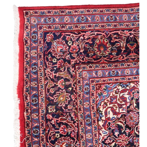 2130 - A RICH RED GROUND PERSIAN KASHAN RUG with dark blue floral patterned central medallion and matc... 