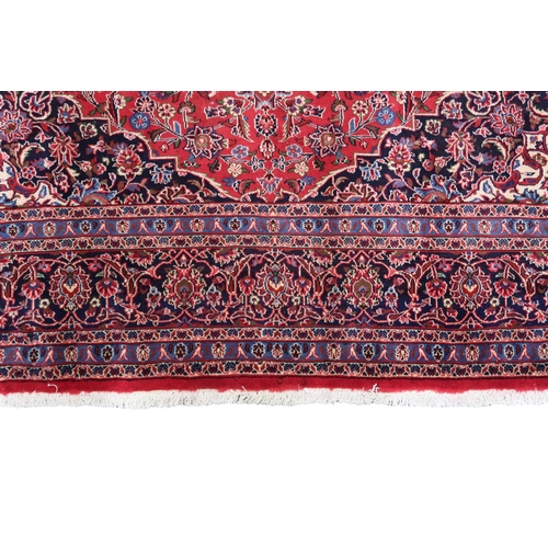 2130 - A RICH RED GROUND PERSIAN KASHAN RUG with dark blue floral patterned central medallion and matc... 