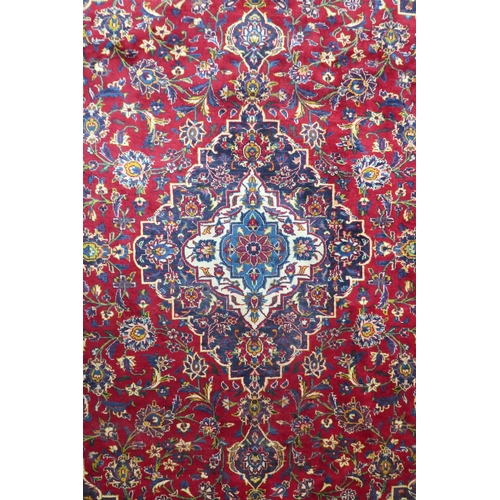 2133 - A RED GROUND IRANIAN TRADITIONAL KASHAN CARPET with dark blue and cream diamond central medalli... 