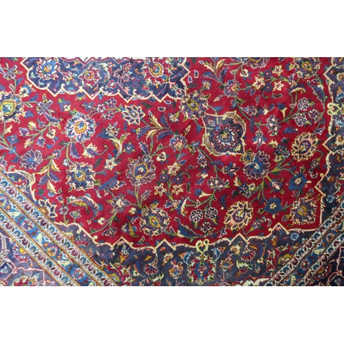 2133 - A RED GROUND IRANIAN TRADITIONAL KASHAN CARPET with dark blue and cream diamond central medalli... 