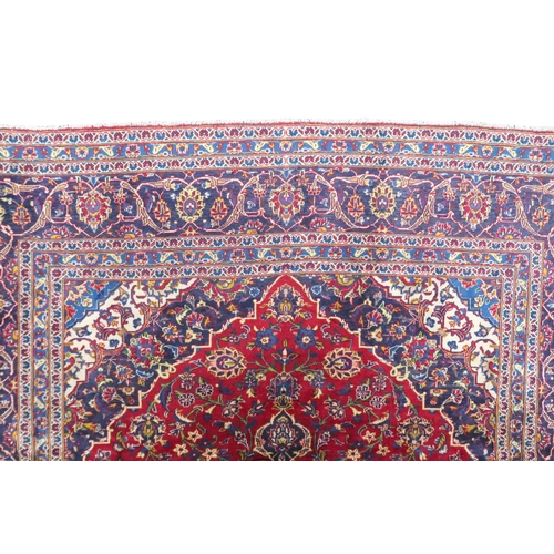 2133 - A RED GROUND IRANIAN TRADITIONAL KASHAN CARPET with dark blue and cream diamond central medalli... 