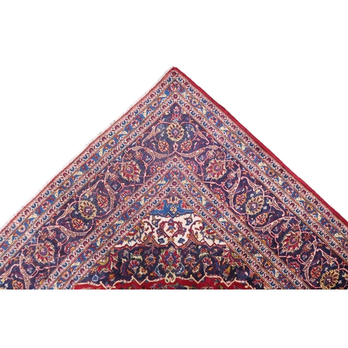 2133 - A RED GROUND IRANIAN TRADITIONAL KASHAN CARPET with dark blue and cream diamond central medalli... 