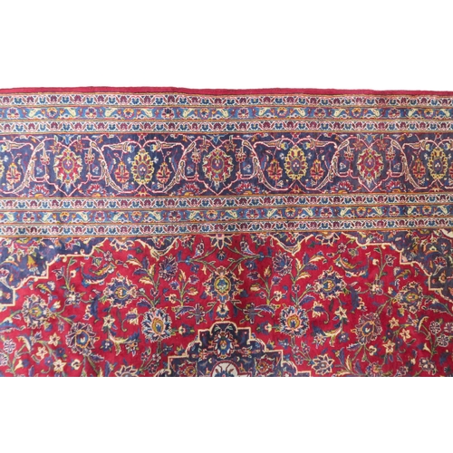 2133 - A RED GROUND IRANIAN TRADITIONAL KASHAN CARPET with dark blue and cream diamond central medalli... 