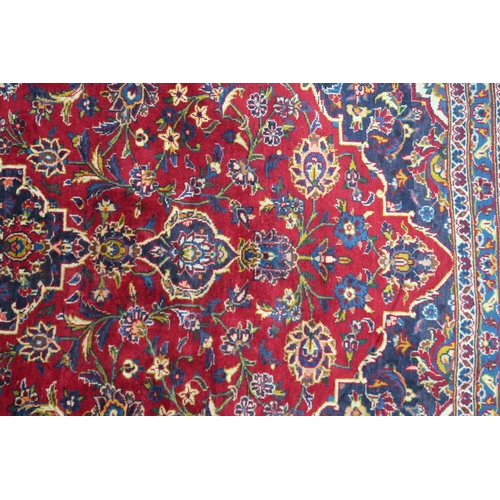 2133 - A RED GROUND IRANIAN TRADITIONAL KASHAN CARPET with dark blue and cream diamond central medalli... 