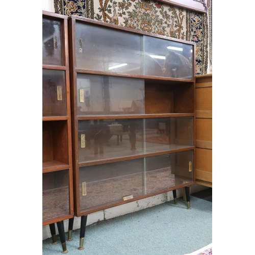 18 - A pair of mid 20th century stained teak bookcases with glass sliding doors on ebonised supports,112c... 