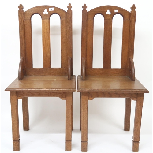 32 - A pair of early 20th century oak ecclesiastical style chairs with pierced trefoil decorations on squ... 