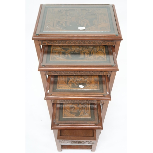 63 - A Chinese nest of four tables, tops carved with village scenes under glass on square supports joined... 