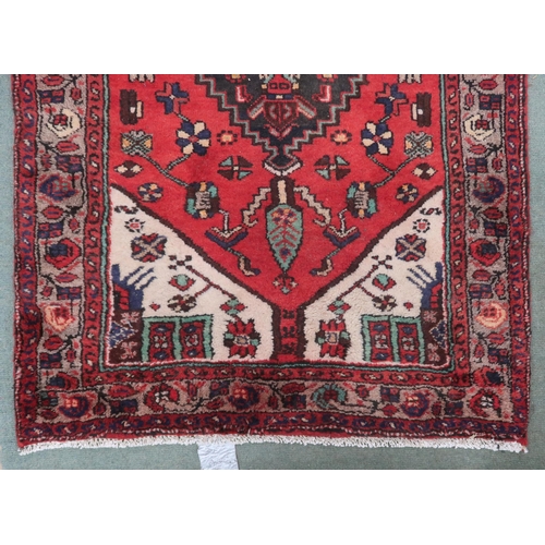 77 - A red ground Persian Hamadan runner with three dark geometric diamond form medallions and cream span... 