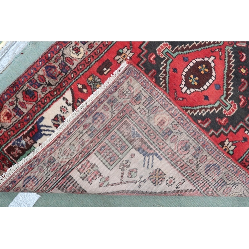 77 - A red ground Persian Hamadan runner with three dark geometric diamond form medallions and cream span... 