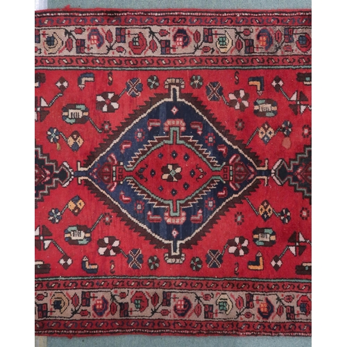 77 - A red ground Persian Hamadan runner with three dark geometric diamond form medallions and cream span... 