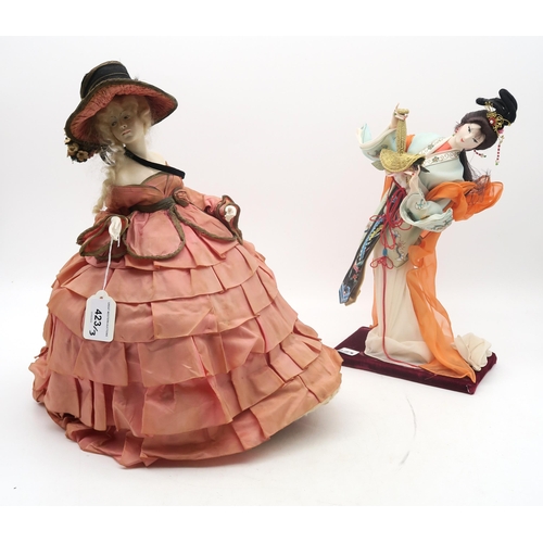 423 - A doll with wearing a well fashioned flounced tea-cosy dress and matching bonnet, a Japanese geisha ... 