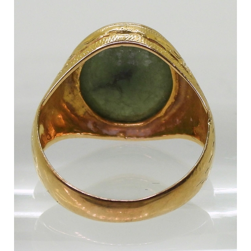 723 - A bright yellow metal signet ring, stamped 90% set with a green hardstone, with engraved shoulders, ... 