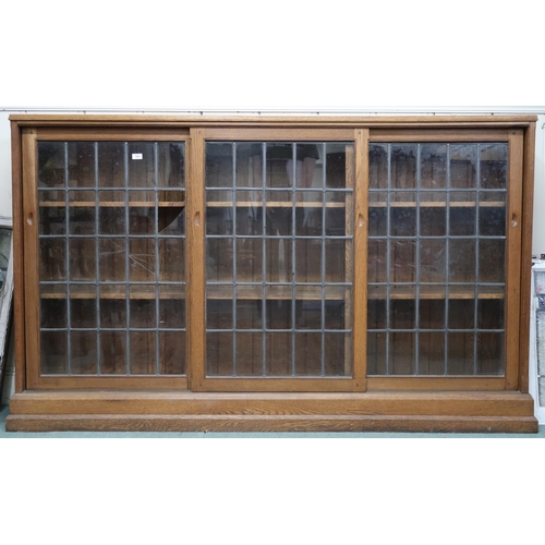 125 - A large early 20th century oak Arts & Crafts bookcase with three leaded glass sliding doors on p... 