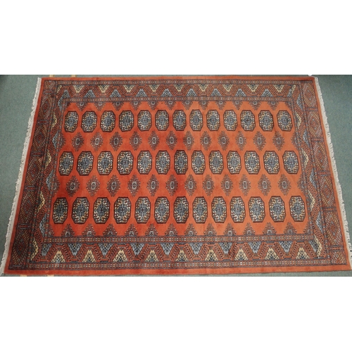 84 - A terracotta ground Bokhara ground rug with all-over lozenge design within multicoloured geometric b... 